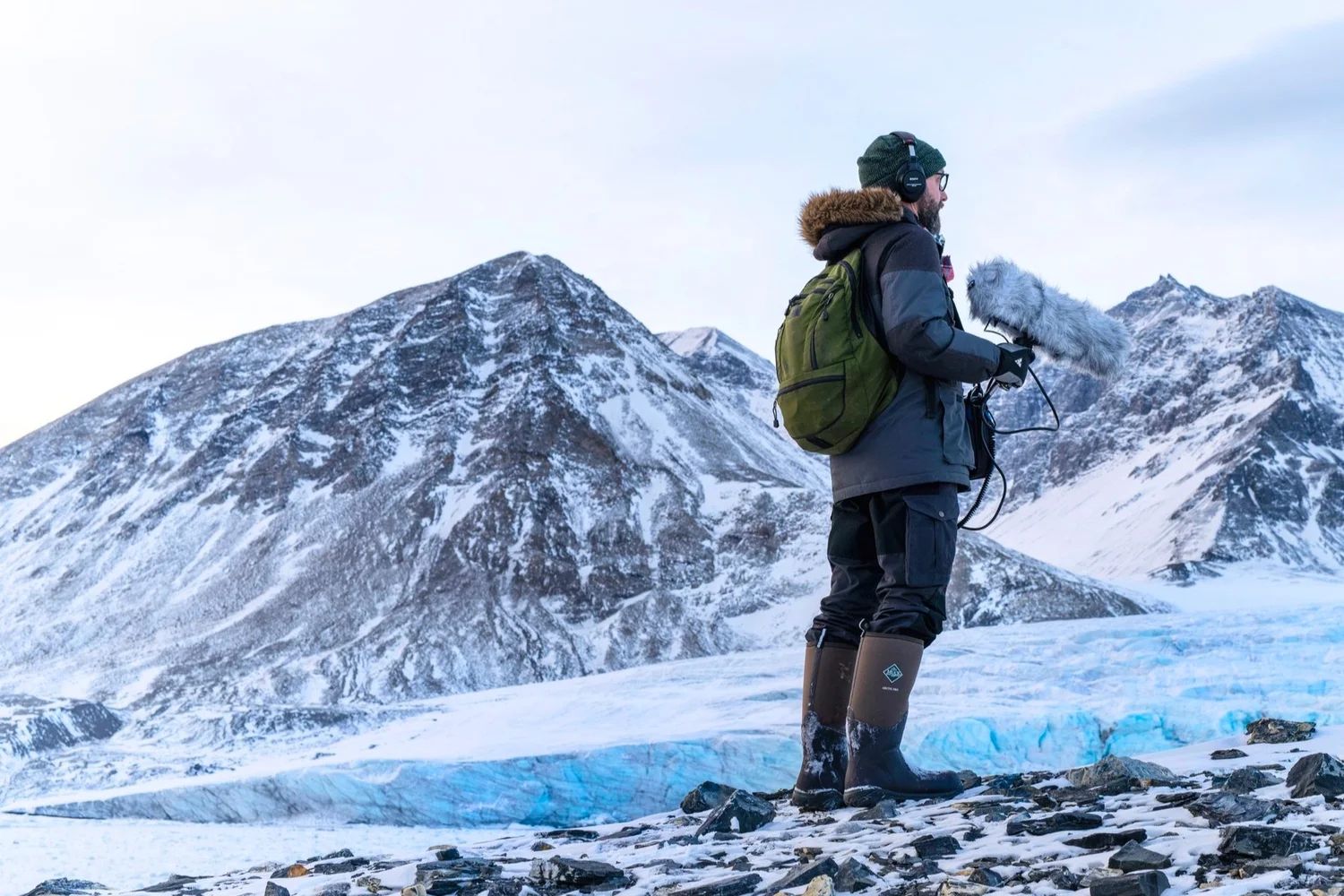 Field recordist holding a microphone in front of snowy mountains in Svalbard